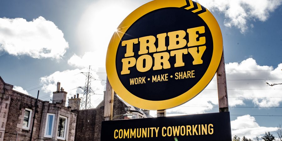 An outdoor sign indiciating Tribe Porty. Underneath is the caption "Work - Make - Share" and "Community Coworking".