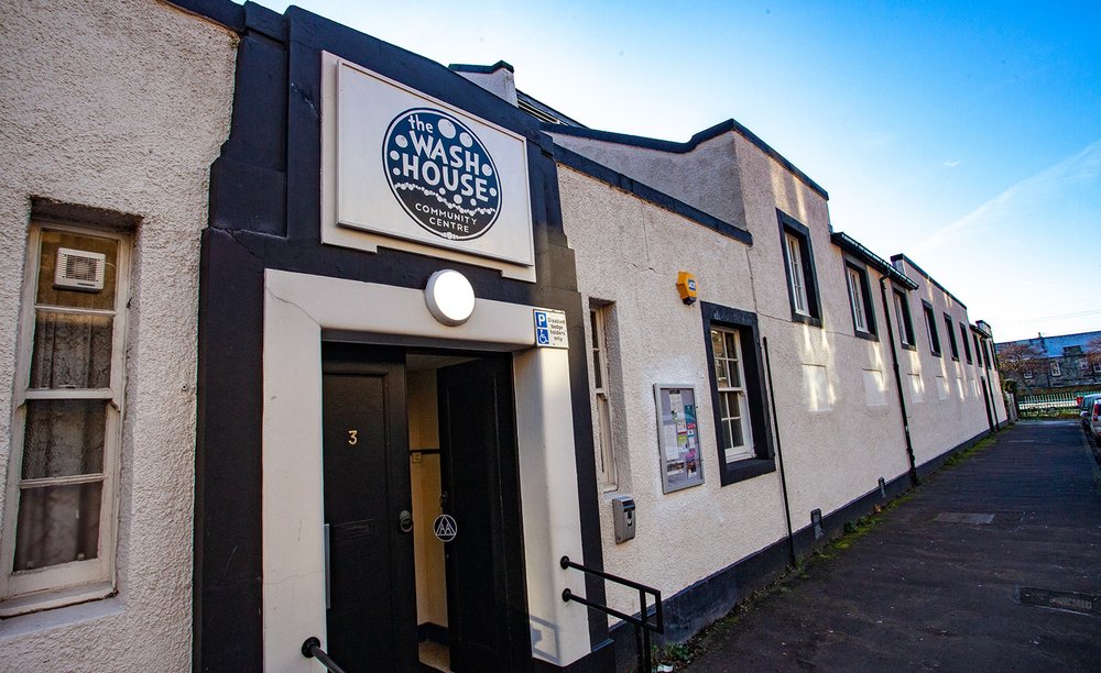The exterior of a building. A sign above the entrace reads The Wash House Community Centre.
